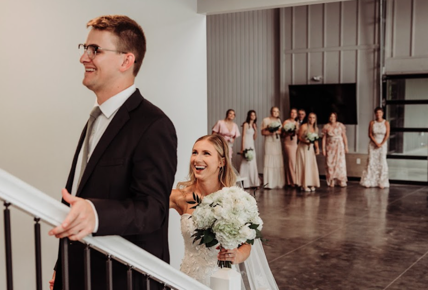 Groom looking upward while standing on stairs with bride behind him and bridal party blurred in the background at Retreat 21 near Columbus, Ohio